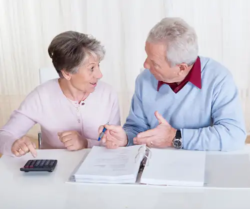 This is a photo of an elderly couple sitting next to each other having a discussion at a table.